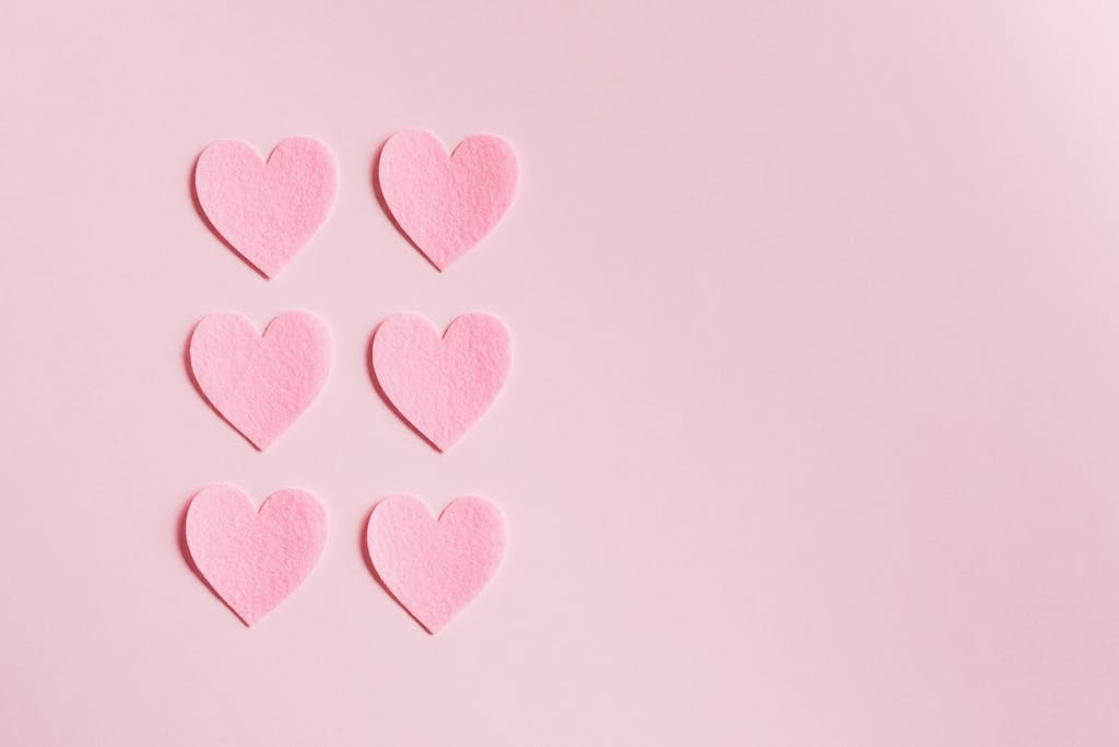 Simple pink heart cutouts arranged on a light pink background, perfect for romantic themes.